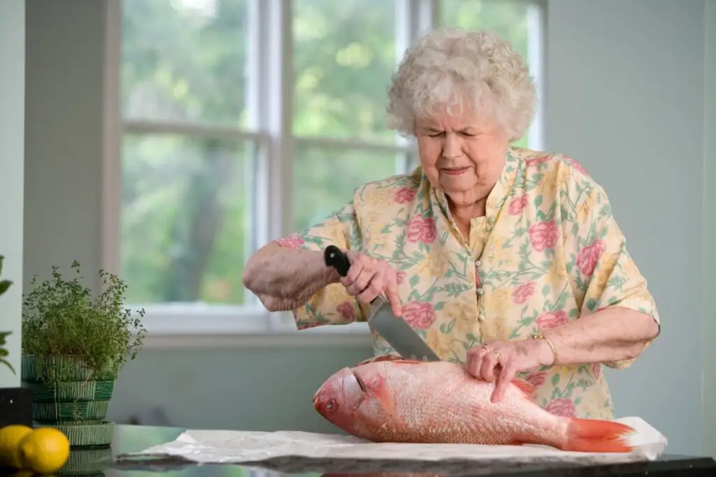an older woman working to prepare meals and/or future frozen meals by fileting a large fish in her own home