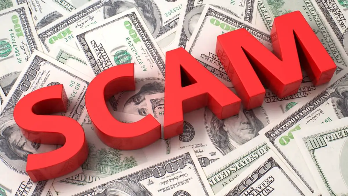 SCAM in red letters on top of a pile of 100 dollar bills