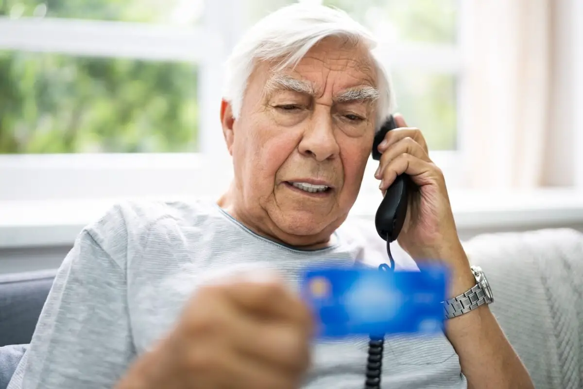Elder man on couch holding phone and credit card, possibly to prevent financial exploitation or elder financial abuse.