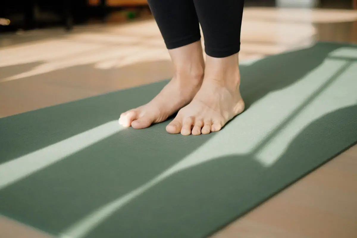 The ankle and toes of a person are visible, standing on a yoga mat.
