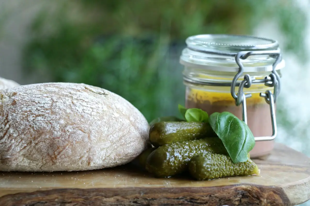 Pate, full of healthy fats, in a glass jar on a wooden board with bread and pickles