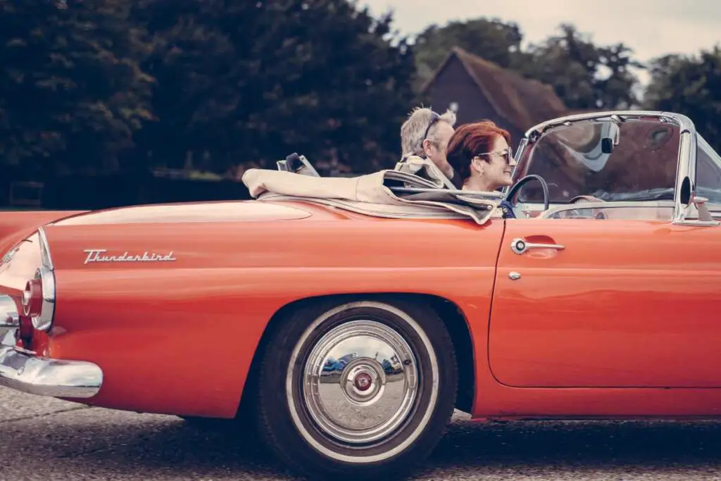 two older adults driving a vintage car while sitting comfortably on car seat cushions
