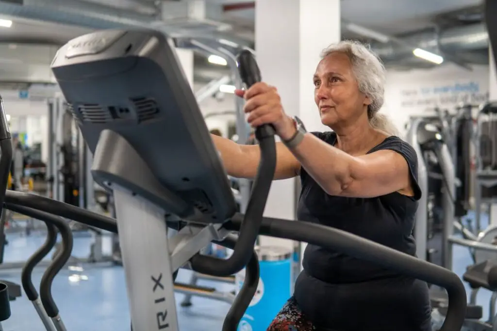 older woman using a cardio machine at the gym, wearing a fitness tracker device on her wrist