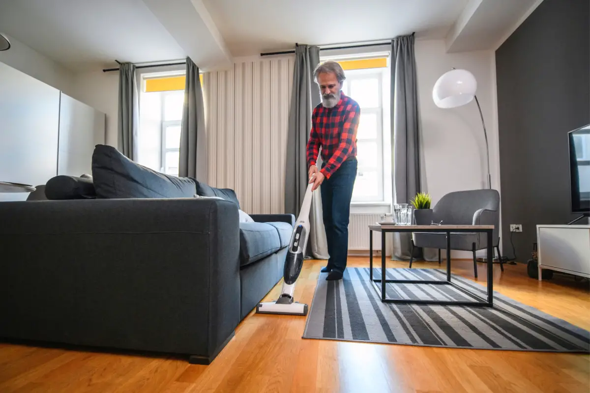 senior man cleaning home using cordless vacuum cleaner on hard floors