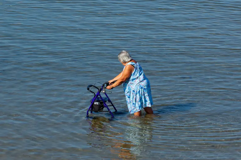 Elderly lady walks with walker in the sea
