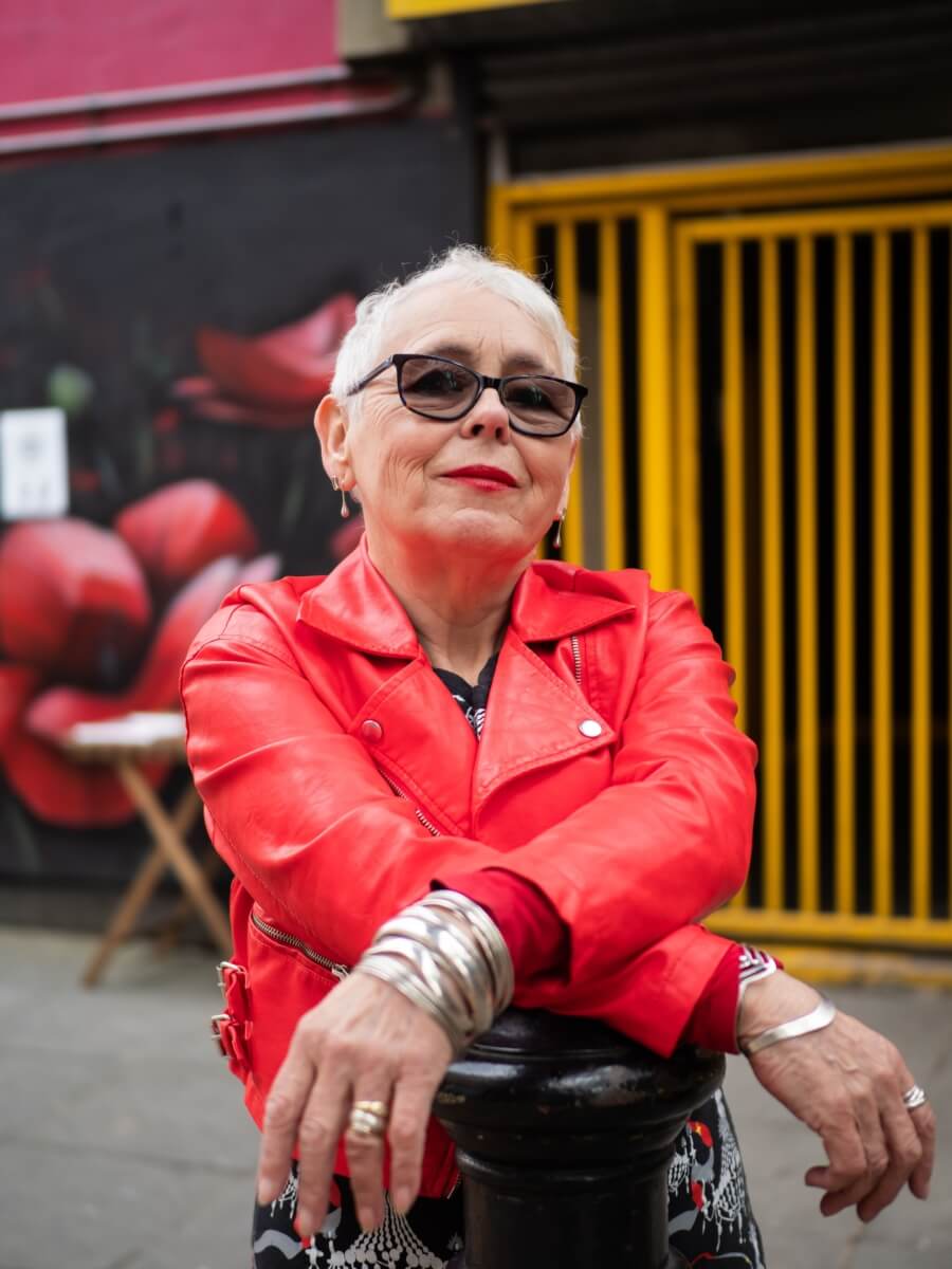 A stylish older woman wearing a red leather jacket and sunglasses.