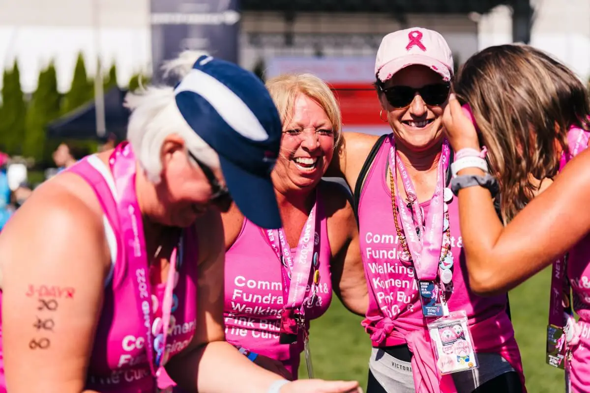 Four older women, all wearing pink, laughing together while wearing sports bras under their event t shirt.