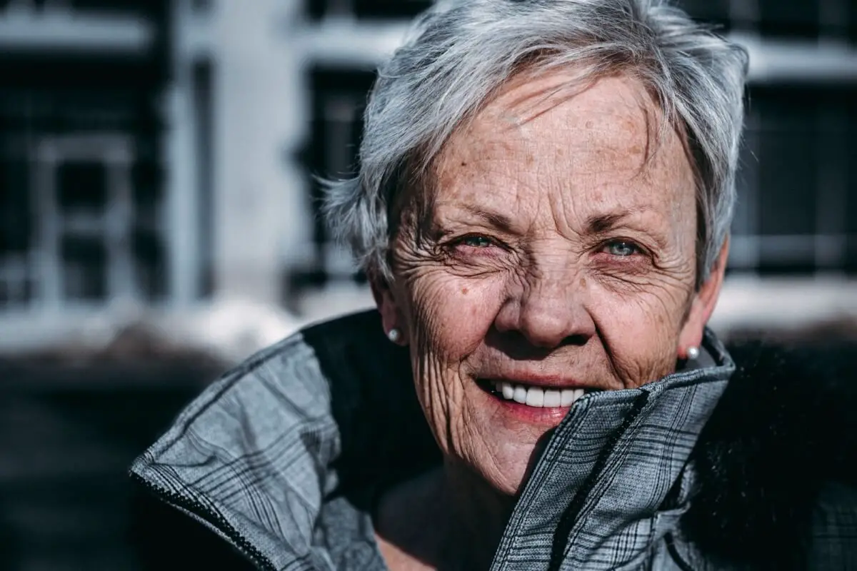 Older woman with short grey hair and kind eyes smiling and looking at the camera.