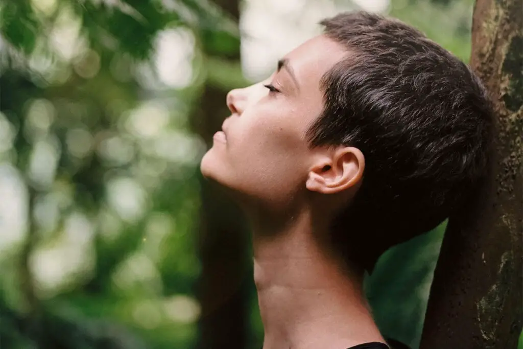 A woman standing next to a tree in a forest