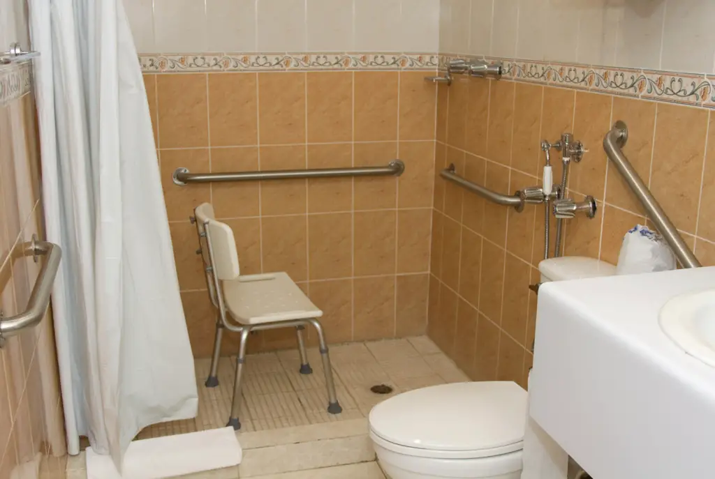 Shower designed for someone with limited mobility featuring a shower transfer chair and multiple shower grab bars