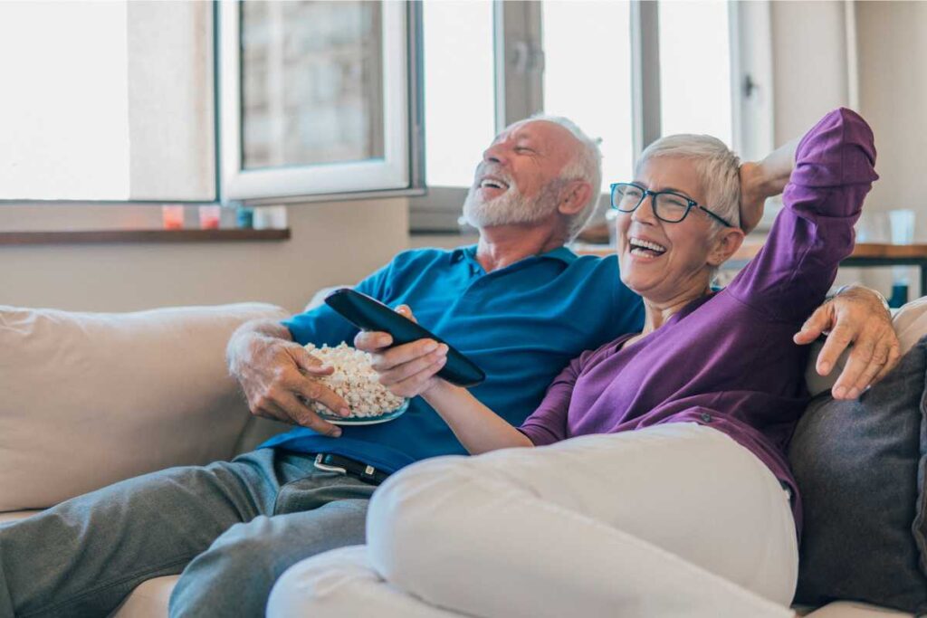 two older adults engaging in physical intimacy via watching a movie together on the couch